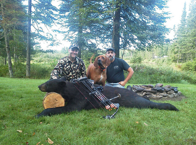 black bear hunter holding kill on stump