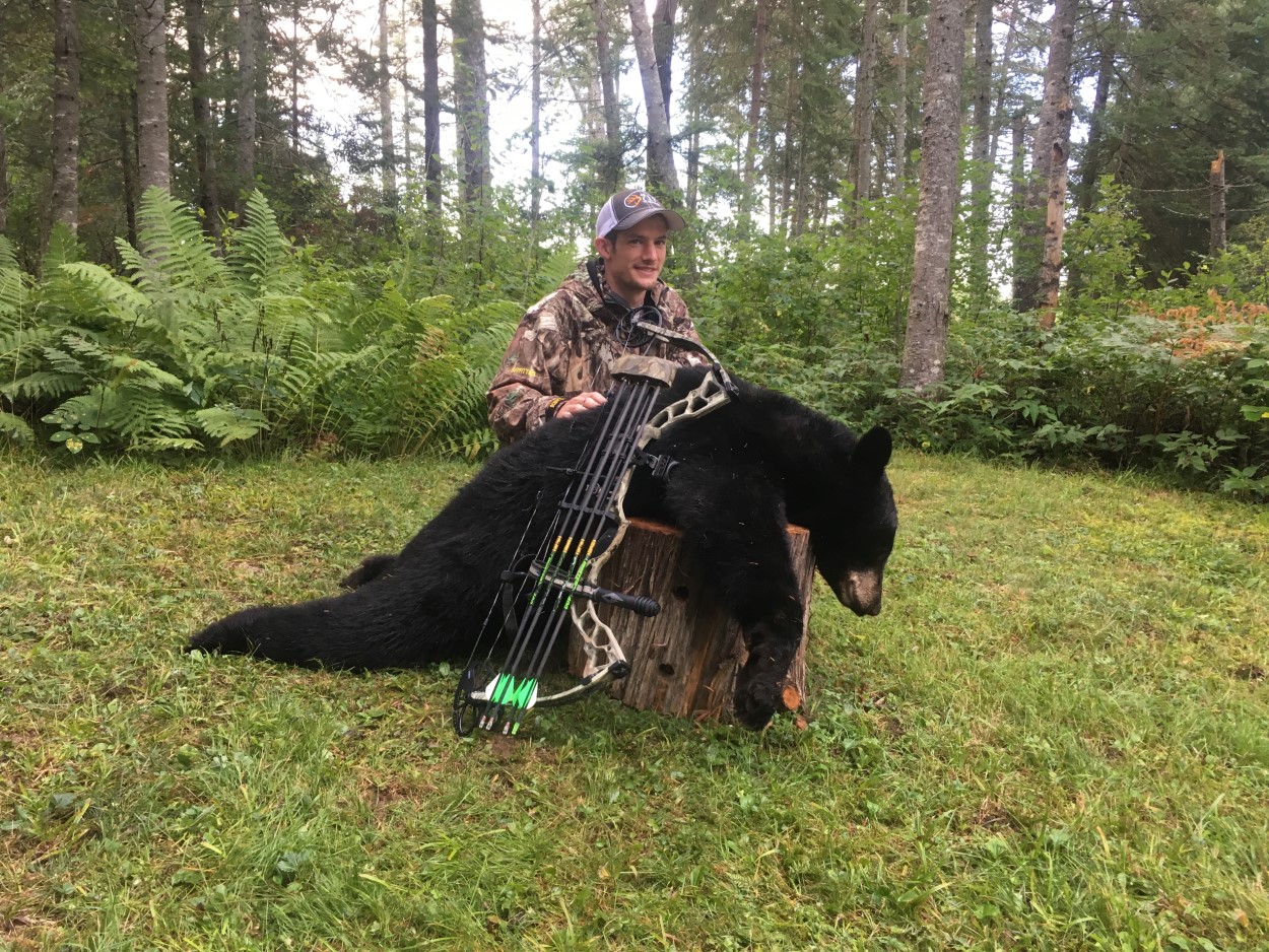 young man posing with bow and killed black bear