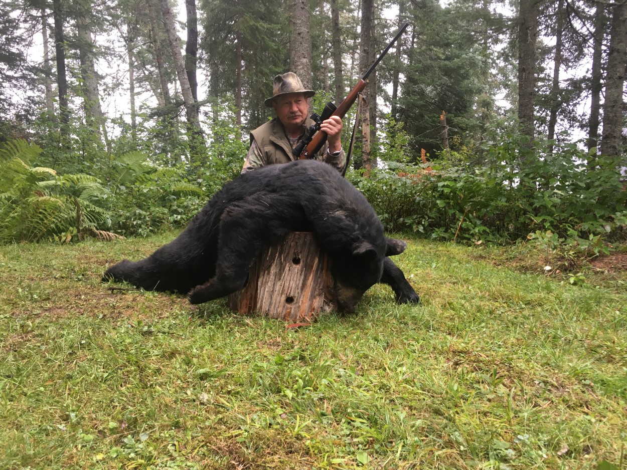 older man posing with rifle and killed black bear