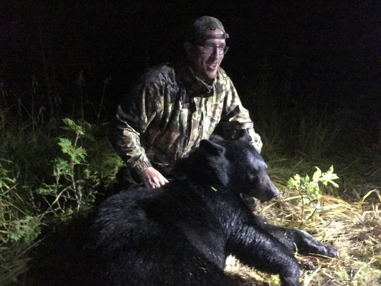 man in dark posing with recently killed black bear