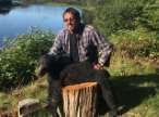 man holding dead black bear cub on wood stump