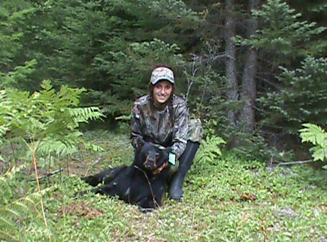 bowhunting woman posing with killed black bear on hunting trip in northern maine