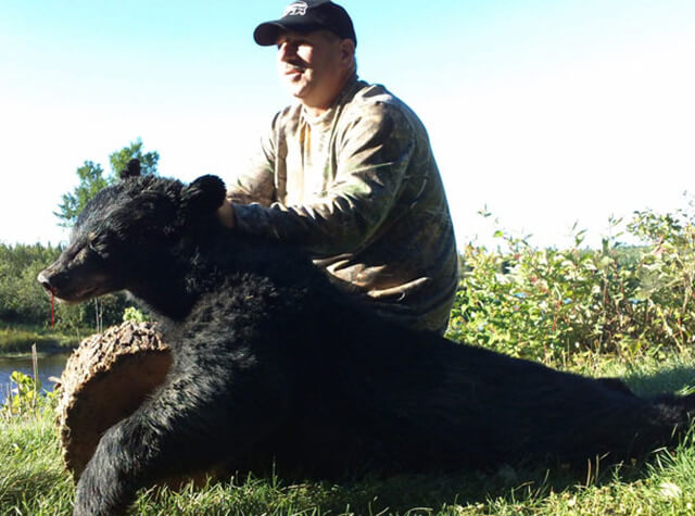 man posing with rifle and killed black bear