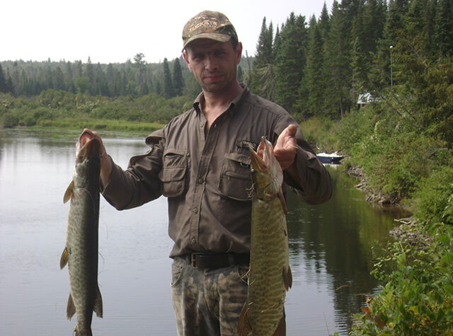 man holding large archery bow and posing with killed black bear 