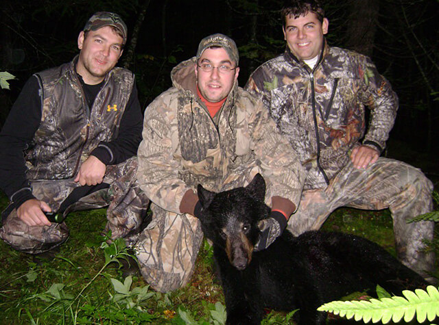 man in hunting gear at night posing with bow and killed black bear
