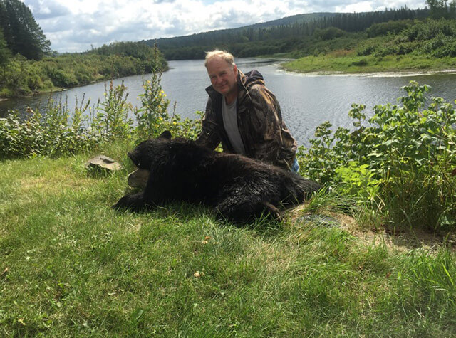 man posing with rilfed and black bear kill
