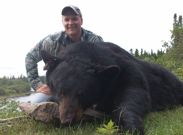 man on hunting trip posing with killed black bear in northern maine
