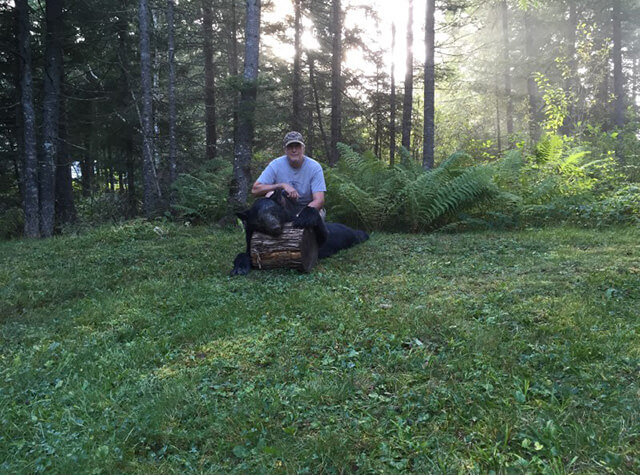 man on hunting trip posing with killed black bear