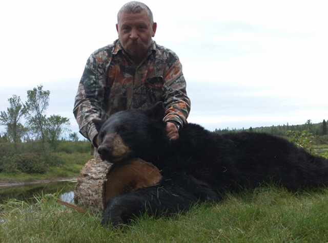 man standing over killed black bear at sunset