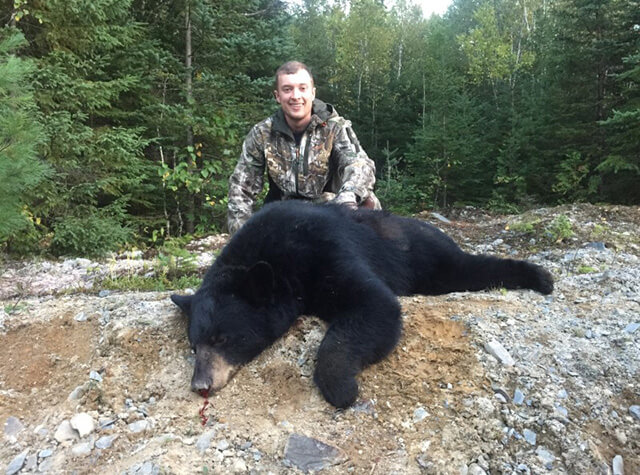 bowhunting man posing with dead black bear on stump